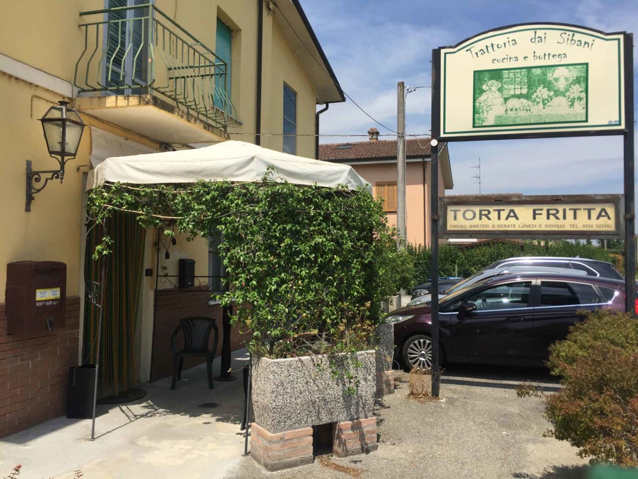 Trattoria dai Sibani a Chiusa Ferranda, Fidenza: l'ingresso preceduto da un piccolo portico e l'insegna con la scritta torta fritta